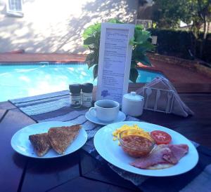 比勒陀利亚Pretoria East Guests的两盘早餐食物放在泳池旁的桌子上
