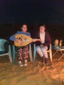 Al WāşilHamood desert local camp的三人坐在沙滩椅上,拿着吉他