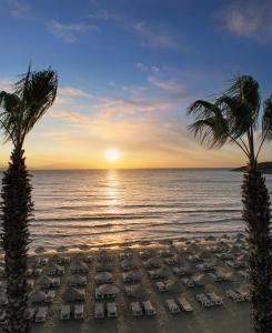 库萨达斯Ramada Hotel & Suites by Wyndham Kusadasi的日落时分带躺椅和棕榈树的海滩