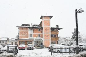 平佐洛Hotel Cristina的一座大型砖砌建筑,汽车停在雪地里