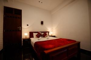 纳拉坦尼亚Adams Peak Inn的一间卧室配有一张带红色床单的床和两盏灯。