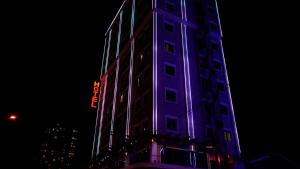 埃尔比勒Hotel Hilen De Ville的一座高大的建筑,晚上有紫色的灯光