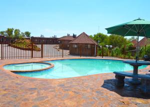 哈博罗内Crocodile Pools Resort的一个带遮阳伞和长凳的游泳池