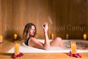 斋沙默尔Desert Dream Royal Camp with Pool的坐在浴缸里拿着一杯葡萄酒的女人