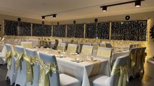 格伦因尼斯Club Hotel的宴会厅配有白色的桌子和带金色弓的椅子
