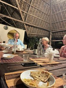 南威Sazani Beach Lodge and Tidal Lounge的一群坐在餐桌上的人,拿着一盘食物