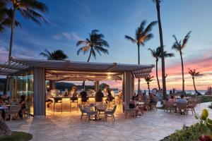 卡胡库Ocean Bungalows at Turtle Bay Resort的天井,人们坐在桌子旁,酒吧在日落时分