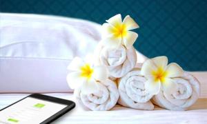 阿吉曼Lotus Furnished Hotel Apartments LLC. Ajman的一组毛巾,床上有鲜花,还有手机