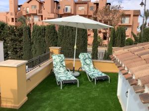 托雷帕切科Mar menor golf detached Villa的阳台配有两把椅子和一把遮阳伞,阳台有草地。