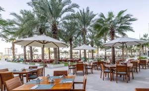 迪拜迪拜朱美拉海滩希尔顿逸林酒店的餐厅设有桌子、遮阳伞和棕榈树。