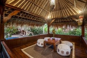 乌布苏哈迪别墅度假屋的一个带椅子和桌子的门廊和茅草屋顶