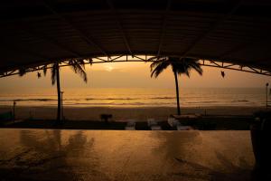 比纳里姆Beach House Resort Goa的海滩上的日落,椅子和棕榈树