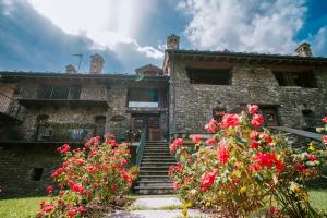 努斯Maison Rosset agriturismo, CAMERE, appartamenti e spa in Valle d'Aosta的一座古老的石头建筑,前面有红花