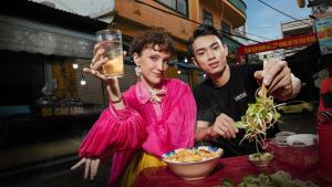 岘港Wink Hotel Danang Riverside - 24hrs Stay & Rooftop with Sunset View的两个人站在桌子边吃着食物和饮料