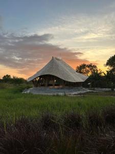 WaikeloMaringi Sumba by Sumba Hospitality Foundation的地里的小屋,背面有日落
