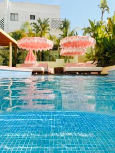 普拉亚登博萨Tropicana Ibiza Suites - Adults Only的一个带两把粉红色遮阳伞和椅子的游泳池