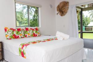 拉罗汤加贝拉海滩简易别墅酒店的白色卧室配有一张带花卉枕头的大床