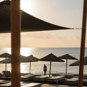 卡马利Afroditi Venus Beach Resort的站在海滩上,拿着椅子和遮阳伞的人