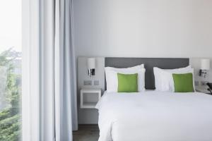 沃韦沃韦公寓式酒店的一张白色的床,窗户旁边配有绿色枕头