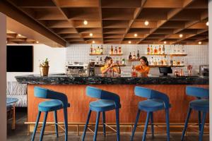 卡兰古特Ronil Goa - a JdV by Hyatt Hotel的两个女人站在一个酒吧后面,酒吧里放着蓝色凳子