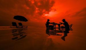 NilandhooHide Inn Blue的两人在日落时坐在海滩上的桌子上