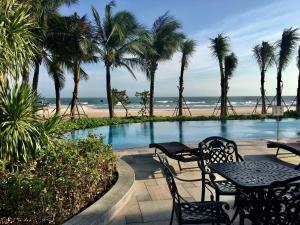 后川Wonderland Villa Hồ Tràm Beach的一个带桌子和棕榈树的游泳池以及海滩