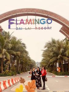 光邝FLAMIGO ĐẠI LẢI RESORT - Villa View Hồ的三个女人站在酒吧入口处的标志下,最后才去