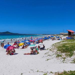 卡波布里奥Locação Temporada Cabo Frio RJ.的一群人坐在海滩上,拿着遮阳伞