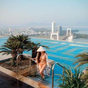 岘港GOLDEN APARTMENT With SEA VIEW的戴帽子的女人站在游泳池旁边