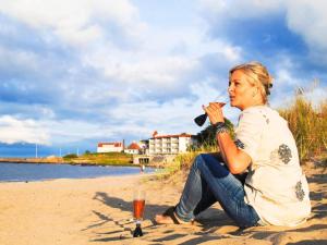 阿灵厄4 person holiday home in Allinge的坐在海滩上喝一杯葡萄酒的女人