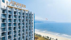 岘港Awaken Da Nang Hotel的海滩上的酒店,天空中放风筝