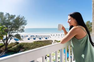 圣徒皮特海滩RumFish Beach Resort by TradeWinds的女人在俯瞰海滩的阳台上喝咖啡