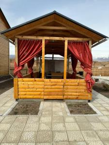 博斯特里WooD_House_Issyk-Kul的木制凉亭,上面有红色窗帘