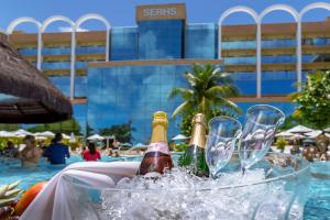 纳塔尔Serhs Natal Grand Hotel & Resort的游泳池畔的2瓶冰香槟和2杯冰香槟
