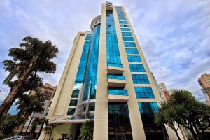 圣保罗Suíte 5 estrelas Hotel Av Ibirapuera 2534 Moema - 1的一座高大的建筑,设有玻璃窗,棕榈树