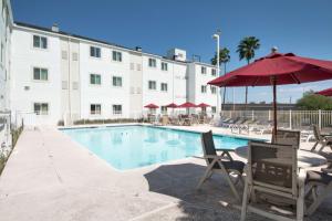 布朗斯维尔Motel 6-Brownsville, TX的一座带椅子和遮阳伞的游泳池位于大楼旁