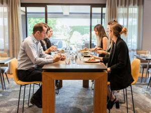 布拉尼亚克铂尔曼图卢兹机场度假酒店的一群人坐在餐馆的桌子旁