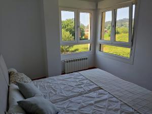 Posada de LlanesApartamento MAR y MONTAÑA ASTURIAS的一间白色卧室,设有2个窗户和1张床