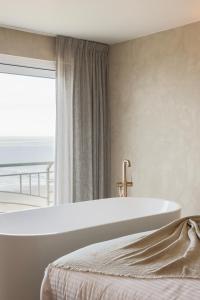 布兰肯贝赫海滩宫廷酒店的卧室设有白色浴缸,卧室设有窗户