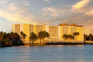 迈阿密迈阿密机场/蓝礁湖霍姆伍德套房酒店的一座棕榈树环绕的大建筑,位于水面前