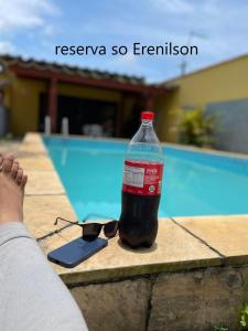 索莱马CASA TEMPORADA PRAIA GRANDE BAIXADA SANTISTA的游泳池畔的一瓶可乐和太阳镜