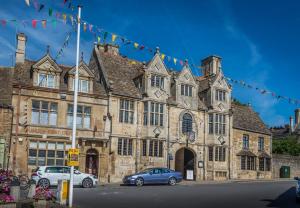 昂德尔The Talbot Hotel, Oundle , Near Peterborough的一座古老的石头建筑,前面有汽车停放