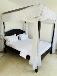 乌昆达Tulivu Suites Diani的白色的天蓬床,配有白色的床单和枕头