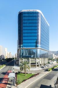 麦加Mercure Makkah Aziziah的一座大型玻璃建筑,前面有一棵棕榈树