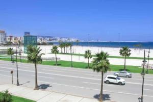 丹吉尔Beautiful Sea View Apartment in Tangier的一条有汽车和棕榈树的街道和海滩