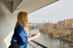 维也纳URBAN ISLAND I Riverside Apartments的站在一个眺望着河流的阳台上的女人