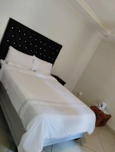 曼齐尼Rest Camp Lodge的一间卧室配有一张白色的床和黑色床头板