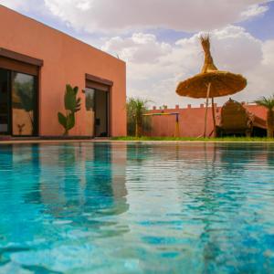 马拉喀什Hotel Jnane riad的一座带遮阳伞的游泳池以及一座建筑