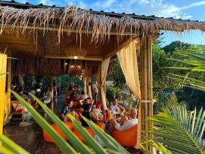 卡塔海滩Greenheart garden View Camp phuket的一群人坐在稻草屋顶下的橙色椅子上