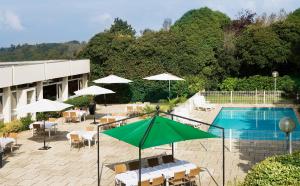 布雷斯特大洋洲布雷斯特机场酒店的一座带桌子和遮阳伞的游泳池,位于一座建筑旁边